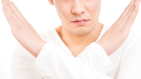 両手をクロスしてバツマークを表現している人物の画像。