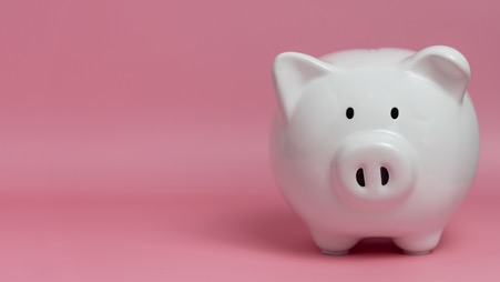 ピンク色の背景に、白いブタの貯金箱。