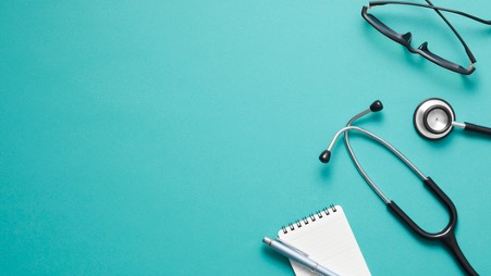 緑色の背景。メモ帳・聴診器・眼鏡が置いてある画像。